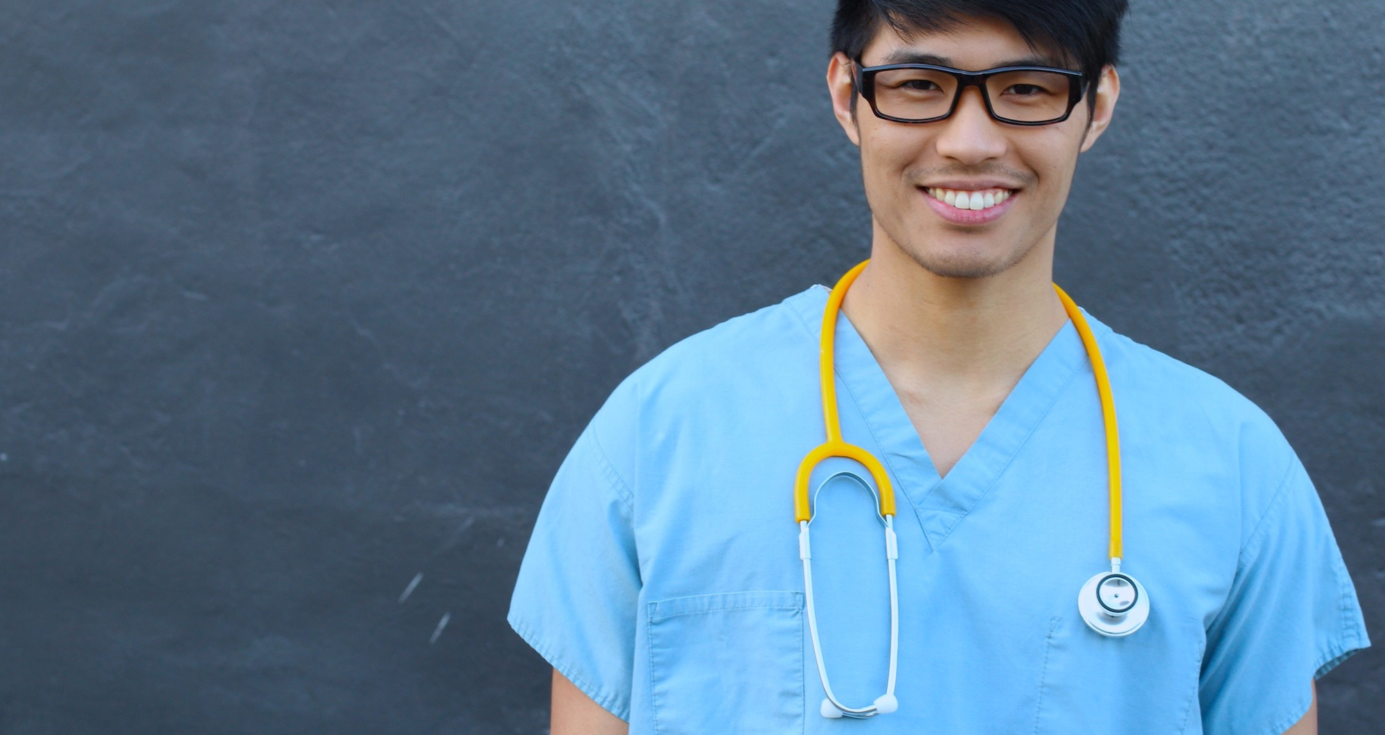 Image shows a happy male student nurse in scrubs smiling directly into camera