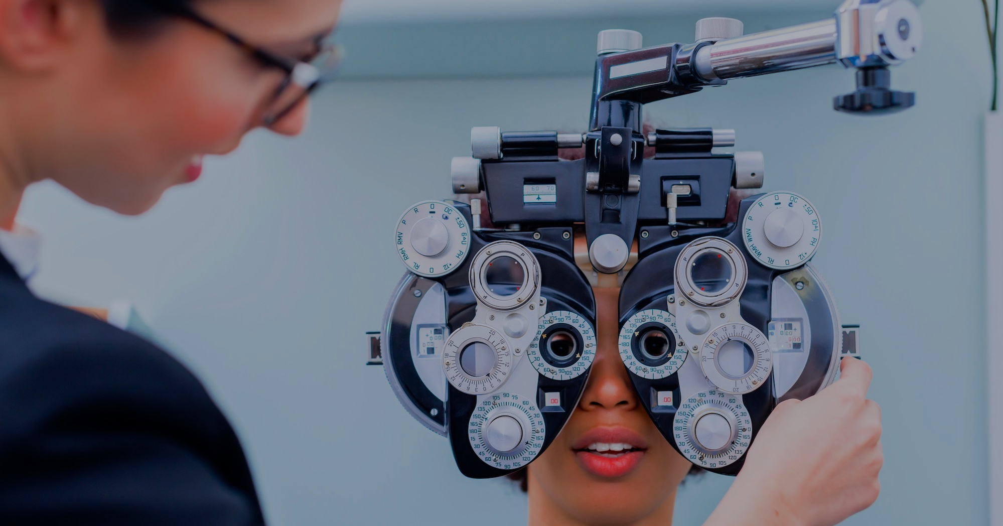 Image shows a woman conducting an eye examination using a phoropter 